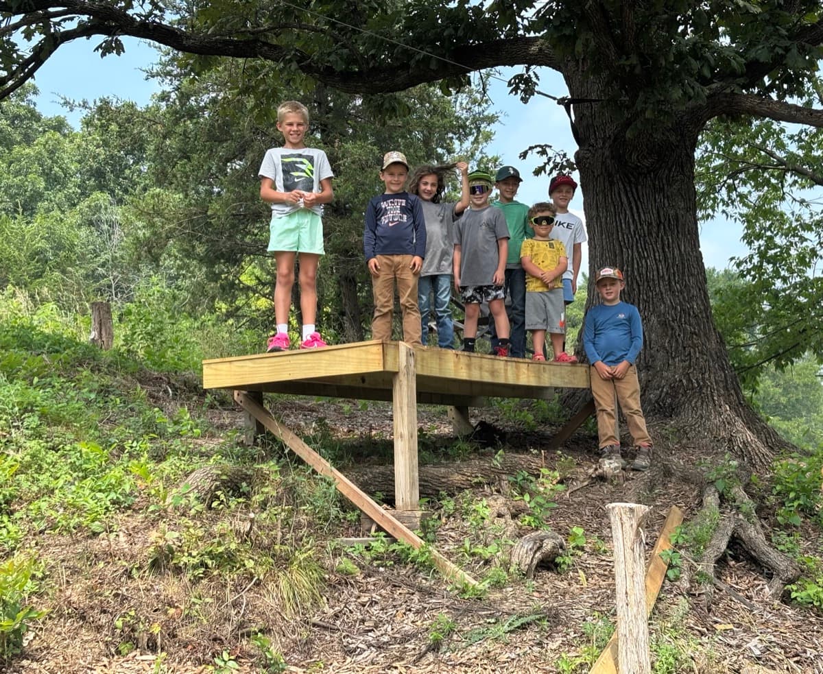 Kids gathered on a wooden platform under a big oak tree
